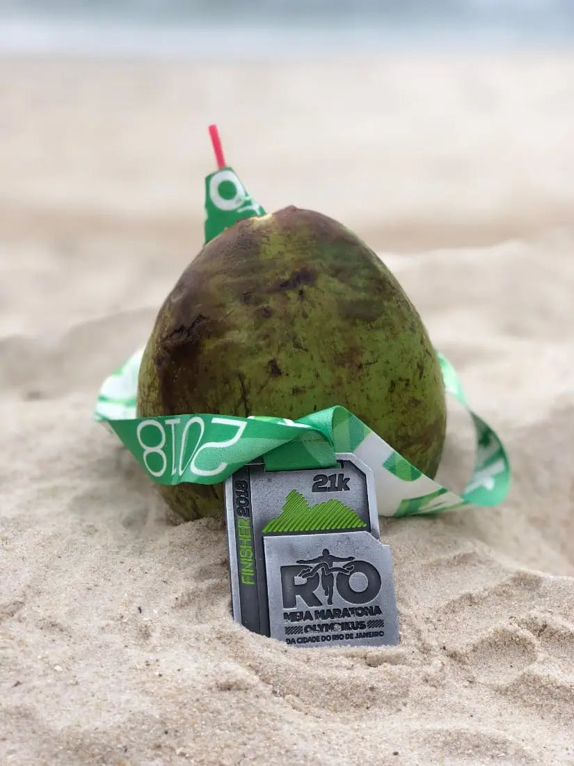 This picture shows a fresh coconut with a straw in it, with a 2018 Maratona do Rio 21km race medal wrapped around it