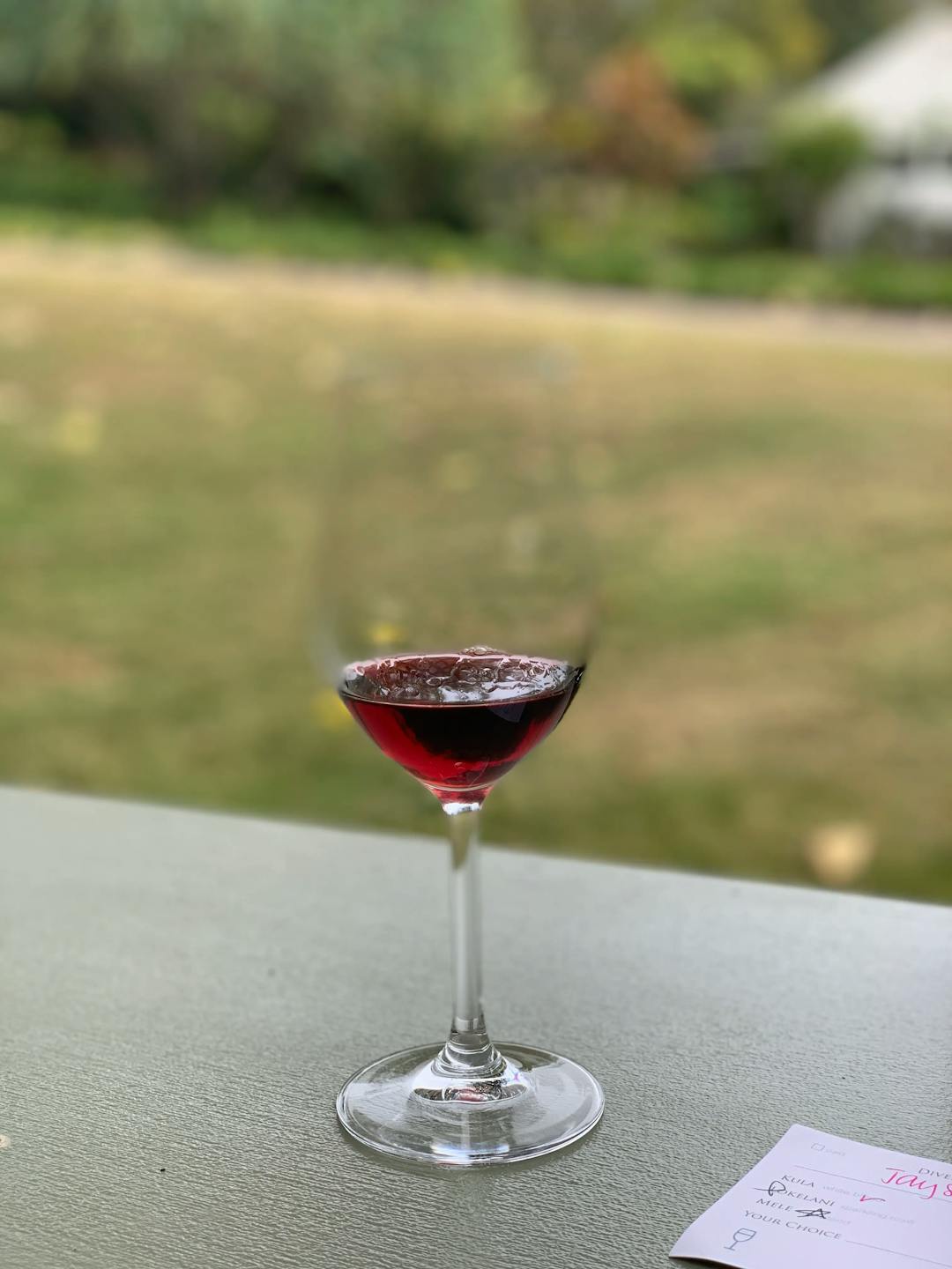 Shot of a glass of red wine, with a lawn in the background
