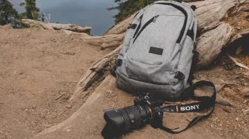 Picture of grey bookbag and sony camera, with forest landscape as the backdrop
